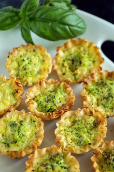 mini pesto quichees on a white plate with basil leaves in the background