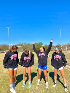 three girls in black sweatshirts standing on grass with their arms up and hands raised