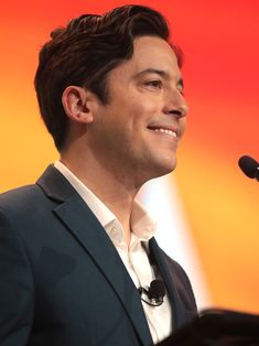 a man standing in front of a microphone and talking into a microphone with an orange background