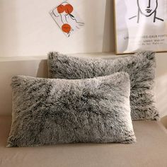 two gray pillows sitting on top of a couch next to a wall with pictures above it