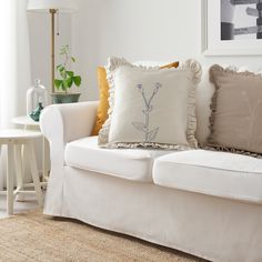 a white couch with pillows on top of it in front of a table and chair