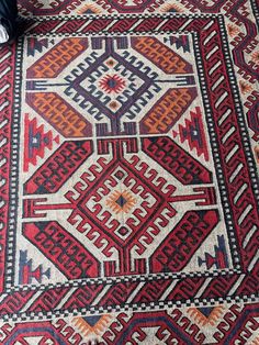 a red and black area rug with an intricate design on the bottom, next to a pair of shoes