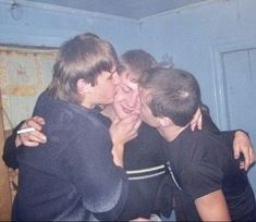 three young men are hugging each other in a room that has blue walls and curtains