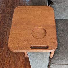 a wooden table sitting on top of a couch next to a gray chair and wood floor