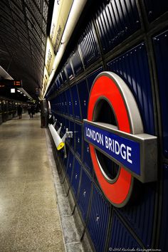 the london bridge sign is attached to the wall in the subway station, with people walking by