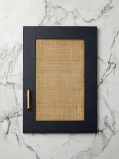 a black frame with a rattan pattern and a gold pen on the side, sitting on a marble surface