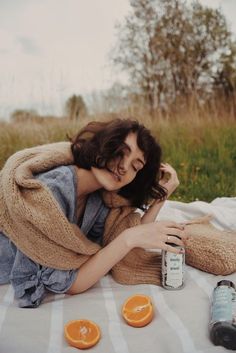 a woman laying on a blanket next to an orange and a bottle of booze