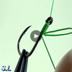 a person is holding a fishing hook with green string attached to it and pointing at the hook