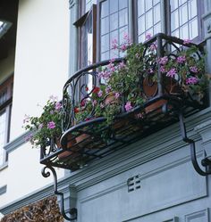 a balcony with flowers and potted plants in the window sill, on top of a building