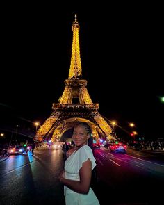 a woman standing in front of the eiffel tower at night with cars passing by