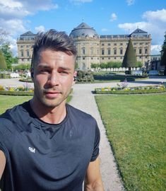 a man taking a selfie in front of a large building with gardens and trees