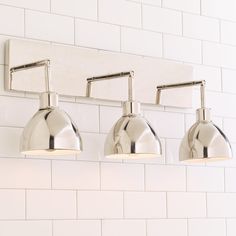 three chrome bathroom lights mounted on a white brick wall