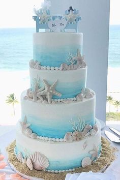 a three tiered cake with blue and white frosting, seashells and starfish