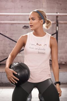 a woman holding a basketball in her right hand and wearing a white tank top that says i am from it, than anybody knows