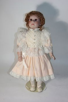 a doll with red hair wearing a pink dress and white lace collared shirt, standing in front of a white background