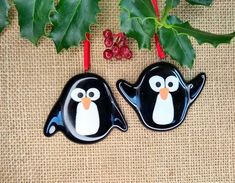 two black and white penguins sitting on top of a table next to holly leaves with red berries