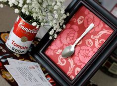 a spoon sits on top of a red and white box with flowers in it next to a can of soup