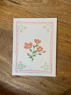 a card with flowers on it sitting on top of a wooden table next to a piece of paper