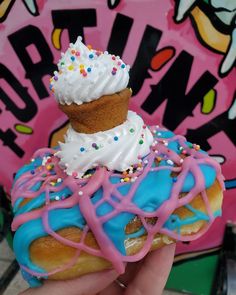 a hand holding a donut with white frosting and sprinkles on it