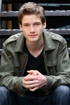 a young man sitting on top of a wooden bench next to a metal rail fence