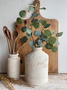 two vases with plants in them sitting on a table next to a cutting board