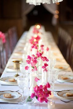 a long table is set with white and pink plates, silverware, and flowers