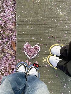 two people standing next to each other on a sidewalk with pink flowers in the background