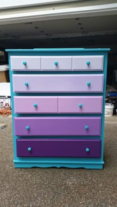 a purple and blue dresser sitting in front of a garage door with the bottom drawer open