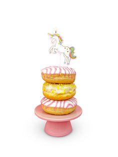 three donuts stacked on top of each other in front of a unicorn cake topper