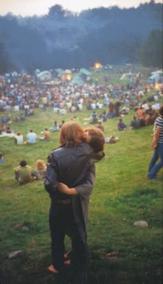 two people hug each other in front of a large group of people sitting on the grass