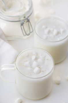 two mugs with marshmallows in them sitting next to a jar of milk