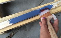 a person holding a paintbrush in their hand and painting the side of a piece of wood