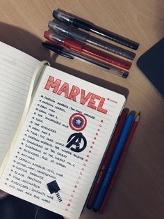 an open notebook sitting on top of a wooden table next to markers and pencils