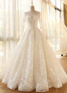 a white wedding dress on display in front of a window with sheer drapes and curtains