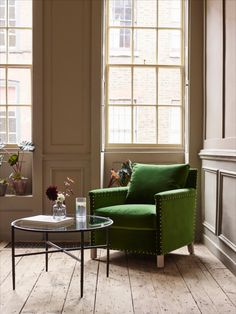 a green chair sitting in front of a window next to a table with flowers on it