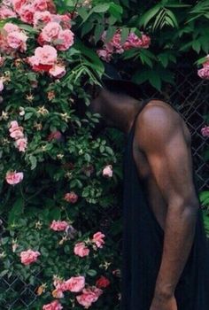 a man standing next to a fence with pink flowers on it