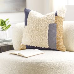 a white couch with two pillows and a book on top of it next to a potted plant