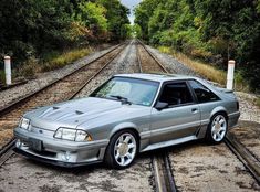 a car that is sitting on some train tracks next to trees and bushes, with the hood down