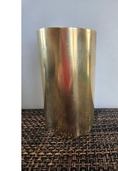 a large metal cup sitting on top of a woven table cloth next to a wall