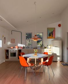 a dining room table with orange chairs around it and an oven in the back ground