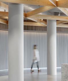 a person walking through an office building with columns and wooden ceiling beams in the background