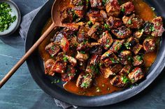 a pan filled with meat covered in sauce and garnished with parsley on the side