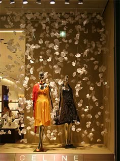 two mannequins dressed in yellow and black dresses with flowers on the wall behind them