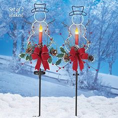 two lighted candles with bows and pine cones on them in the snow, set of 2