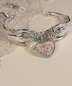 a bracelet with a heart shaped charm on it next to a lace covered table cloth