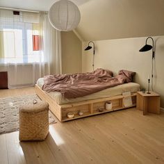 a bed sitting on top of a hard wood floor next to a lamp and window