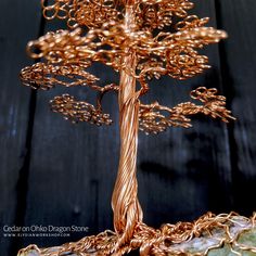 a gold wire tree sculpture sitting on top of a wooden table next to a rock