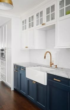 a white kitchen with blue cabinets and gold faucet in the sink, along with wood flooring