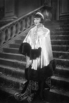 an old photo of a woman in costume standing on the steps with her coat over her shoulders