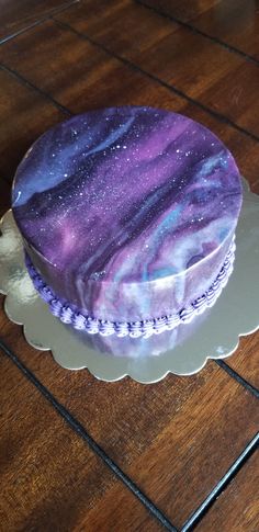 a purple and blue cake sitting on top of a wooden table next to a white plate